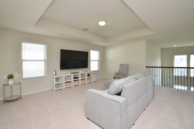 living room with plenty of natural light, light carpet, and a tray ceiling