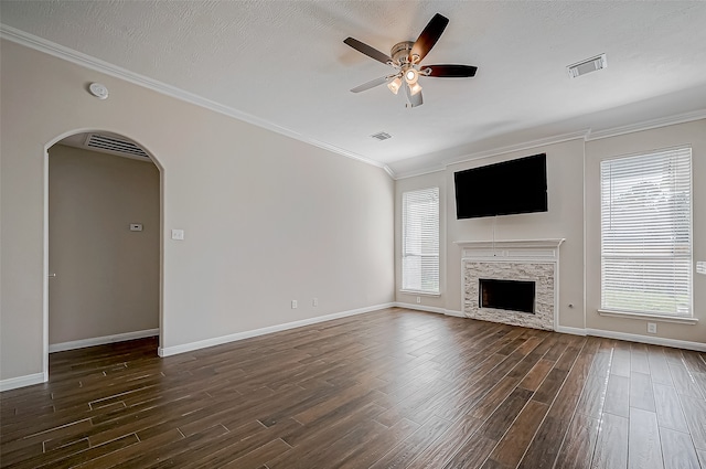 unfurnished living room with a stone fireplace, dark hardwood / wood-style floors, ceiling fan, ornamental molding, and a textured ceiling