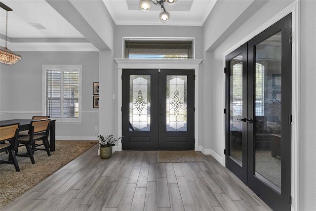 foyer entrance with a notable chandelier, light hardwood / wood-style floors, ornamental molding, and french doors