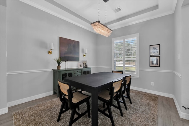 dining room featuring a chandelier, a raised ceiling, light hardwood / wood-style flooring, and crown molding