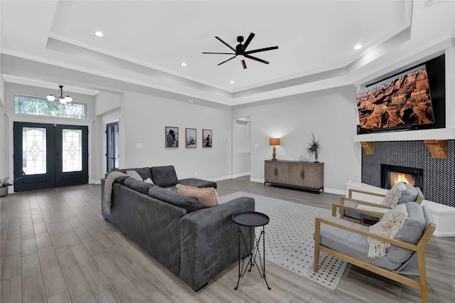 living room featuring a raised ceiling, a fireplace, ornamental molding, and light wood-type flooring