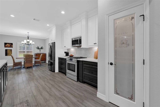 kitchen featuring crown molding, light hardwood / wood-style floors, decorative light fixtures, white cabinets, and appliances with stainless steel finishes