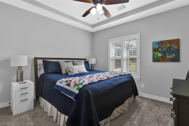 bedroom with a raised ceiling, ceiling fan, and light colored carpet