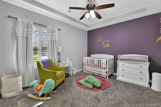 bedroom with a tray ceiling, ceiling fan, carpet flooring, and a crib