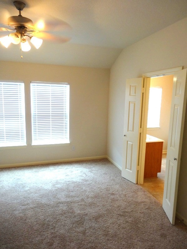 carpeted spare room with ceiling fan and vaulted ceiling