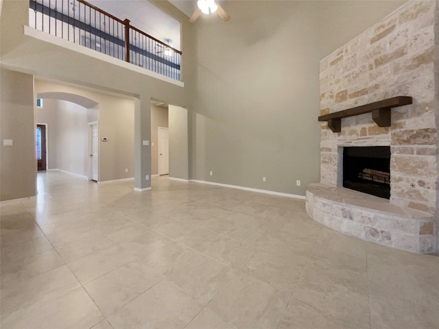 unfurnished living room featuring ceiling fan, a fireplace, and a towering ceiling