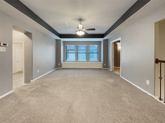 empty room with a tray ceiling, light carpet, and ceiling fan