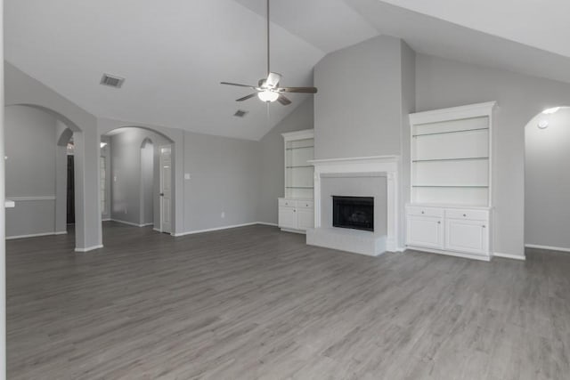 unfurnished living room with ceiling fan, lofted ceiling, a fireplace, wood-type flooring, and built in shelves