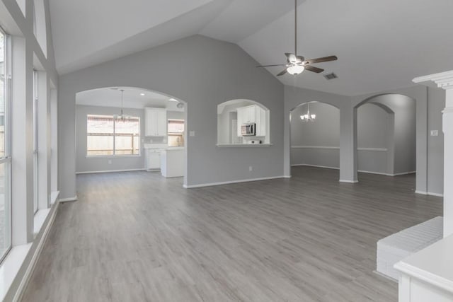 unfurnished living room featuring lofted ceiling, ceiling fan with notable chandelier, and hardwood / wood-style flooring