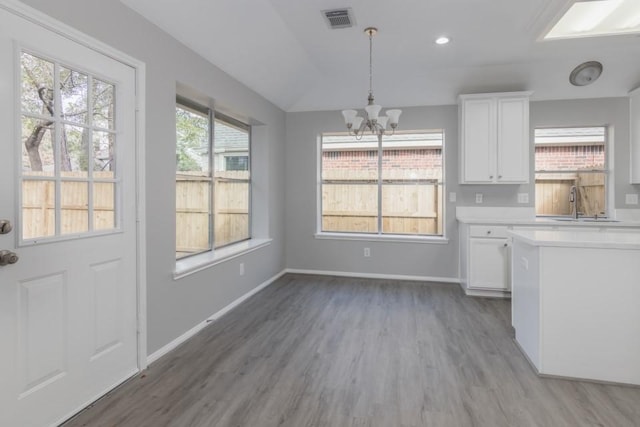 unfurnished dining area featuring vaulted ceiling, sink, wood-type flooring, and a notable chandelier