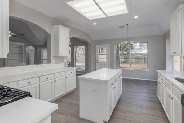 kitchen with a kitchen island, lofted ceiling, white cabinets, and hanging light fixtures