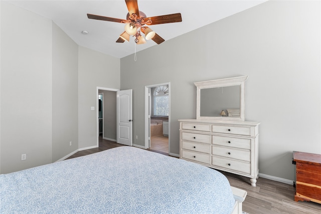 bedroom featuring baseboards, a ceiling fan, ensuite bath, wood finished floors, and high vaulted ceiling