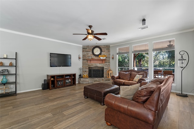 living area with visible vents, ornamental molding, a stone fireplace, wood finished floors, and baseboards