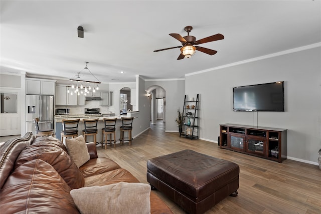 living room featuring ornamental molding, arched walkways, baseboards, and wood finished floors