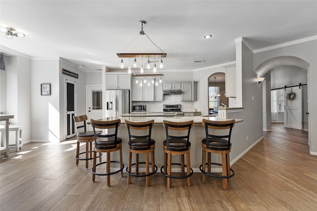 kitchen with gray cabinetry, stainless steel appliances, a barn door, light hardwood / wood-style flooring, and crown molding