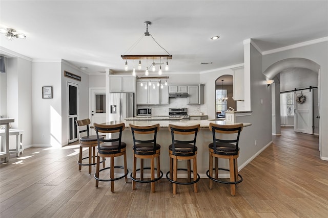 kitchen featuring arched walkways, stainless steel appliances, gray cabinets, light countertops, and a barn door