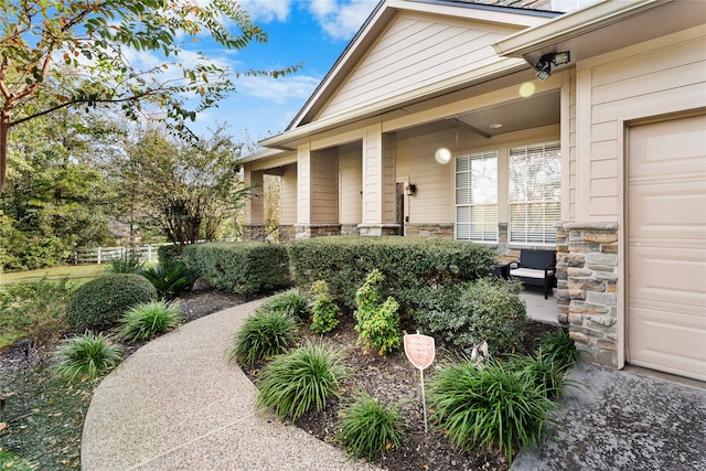 doorway to property featuring stone siding, fence, and an attached garage