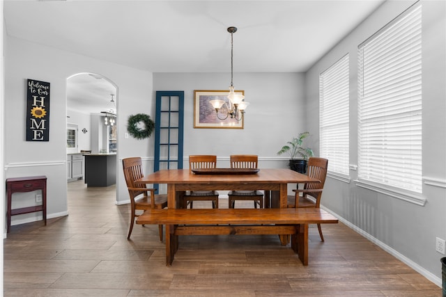 dining space with arched walkways, baseboards, wood finished floors, and a notable chandelier