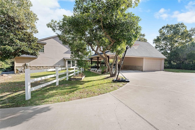 view of front of home featuring stone siding, fence, concrete driveway, and a front yard