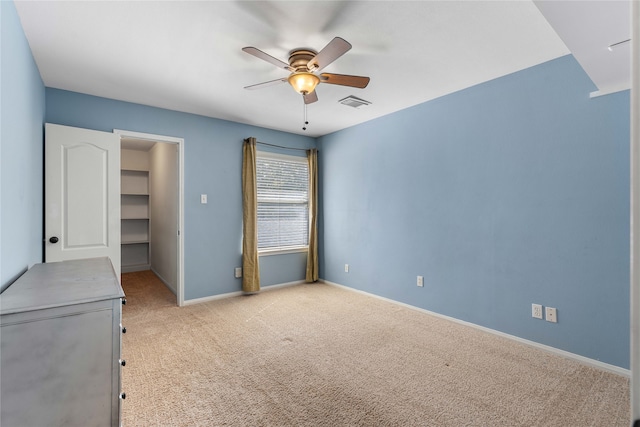 unfurnished bedroom featuring ceiling fan, light colored carpet, visible vents, baseboards, and a walk in closet