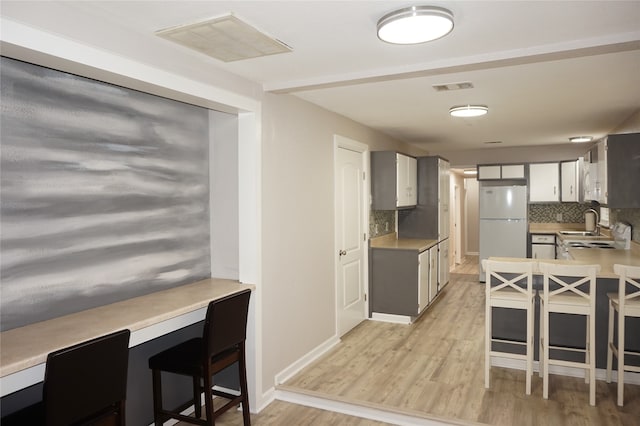 kitchen featuring backsplash, sink, light hardwood / wood-style flooring, white fridge, and a breakfast bar area