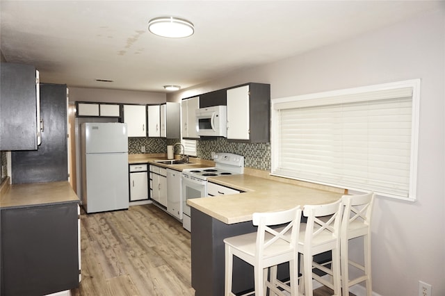 kitchen featuring sink, tasteful backsplash, white appliances, white cabinets, and light wood-type flooring