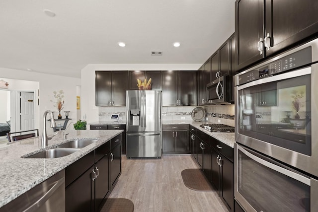 kitchen featuring dark brown cabinetry, sink, stainless steel appliances, light hardwood / wood-style floors, and decorative backsplash