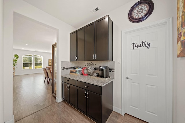 kitchen featuring dark brown cabinets, light hardwood / wood-style floors, and decorative backsplash