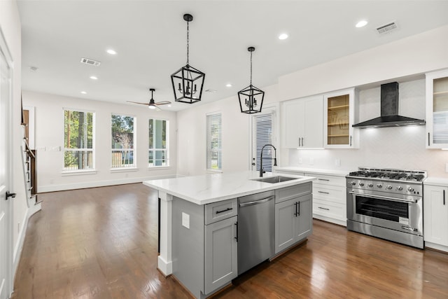 kitchen with a center island with sink, sink, wall chimney exhaust hood, ceiling fan, and stainless steel appliances