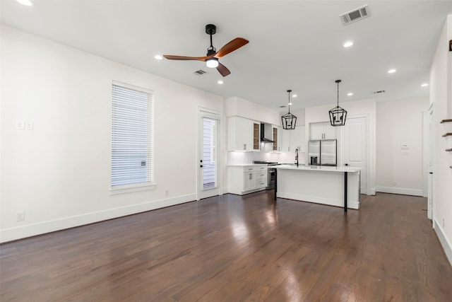 kitchen with pendant lighting, a center island with sink, white cabinets, wall chimney range hood, and appliances with stainless steel finishes