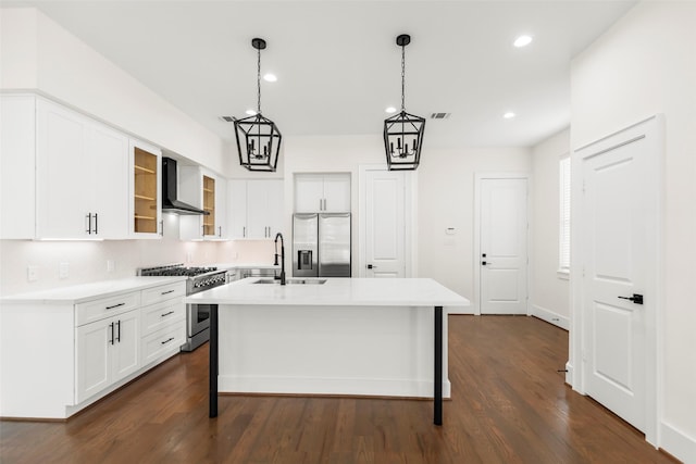 kitchen with pendant lighting, wall chimney range hood, dark hardwood / wood-style floors, an island with sink, and appliances with stainless steel finishes