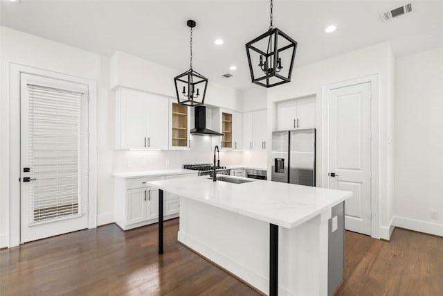 kitchen with pendant lighting, a center island with sink, stainless steel refrigerator with ice dispenser, wall chimney exhaust hood, and white cabinetry