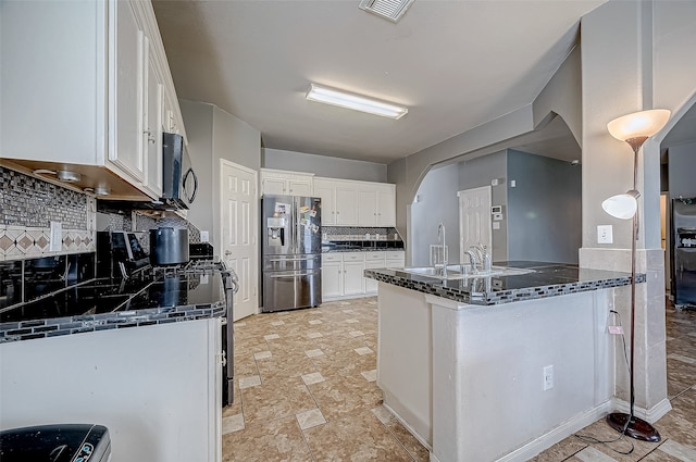 kitchen with kitchen peninsula, dark stone countertops, decorative backsplash, white cabinets, and appliances with stainless steel finishes