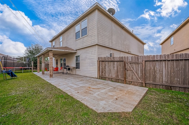 rear view of house with a trampoline, a patio, and a yard