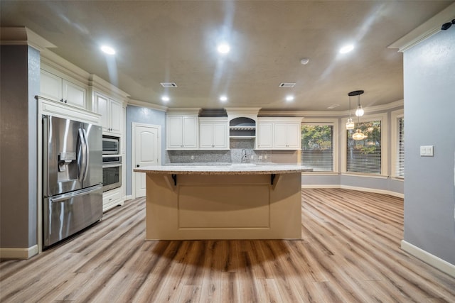 kitchen with white cabinetry, hanging light fixtures, stainless steel appliances, tasteful backsplash, and an island with sink