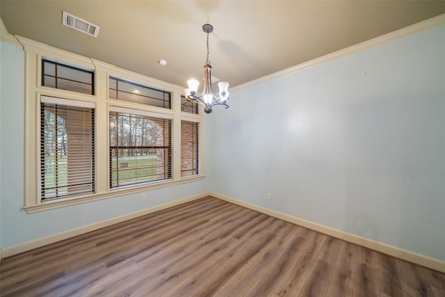 spare room with wood-type flooring, crown molding, and a notable chandelier