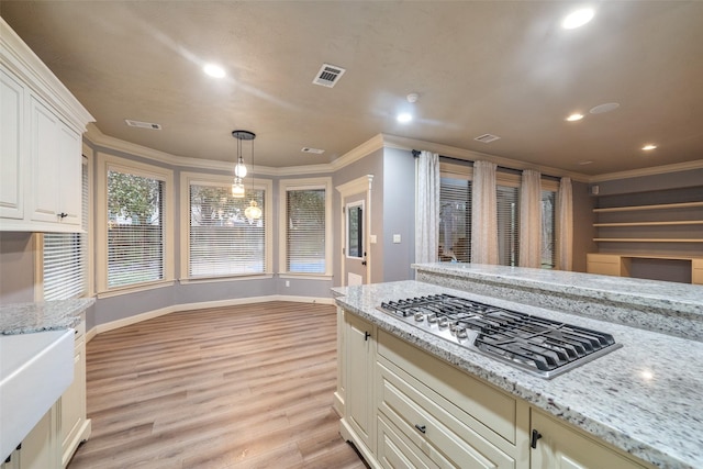 kitchen featuring crown molding, hanging light fixtures, light wood-type flooring, light stone countertops, and stainless steel gas cooktop