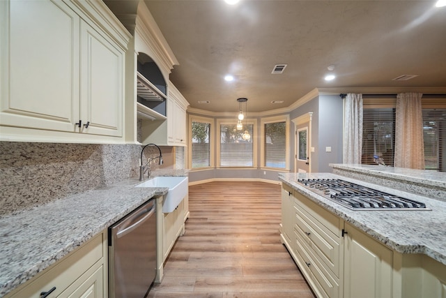 kitchen with light stone counters, cream cabinets, stainless steel appliances, and decorative light fixtures