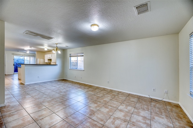 tiled empty room with a textured ceiling and a notable chandelier