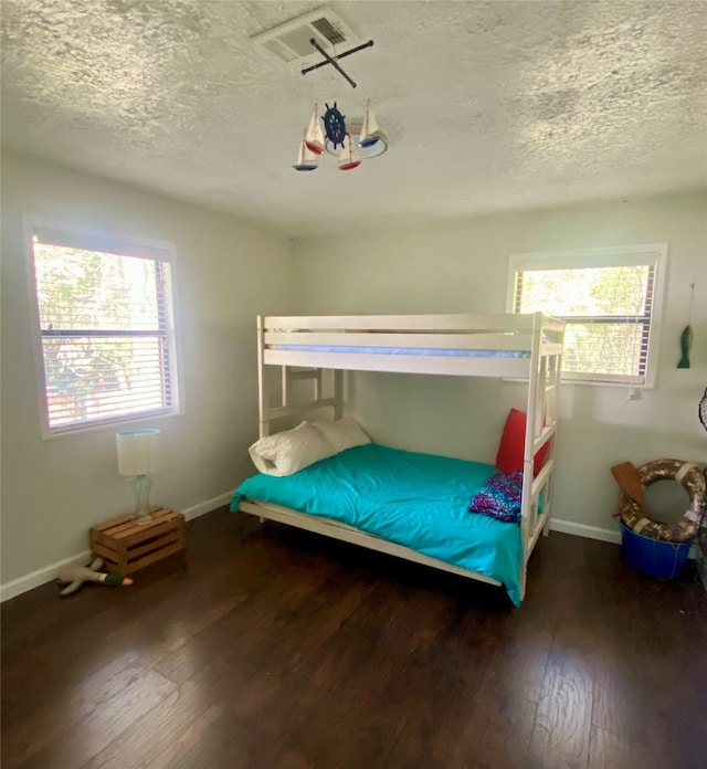 bedroom with a textured ceiling, dark hardwood / wood-style floors, and multiple windows