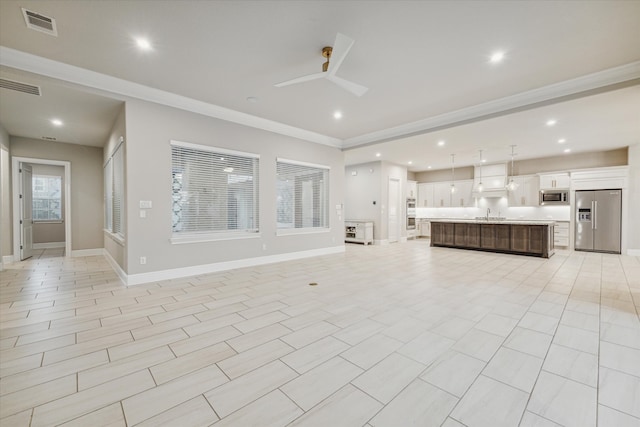 unfurnished living room with ceiling fan, sink, and crown molding