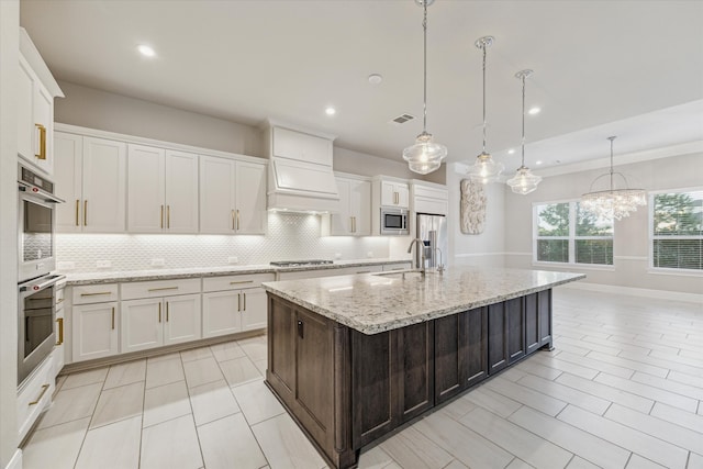 kitchen featuring decorative light fixtures, white cabinetry, an island with sink, and appliances with stainless steel finishes