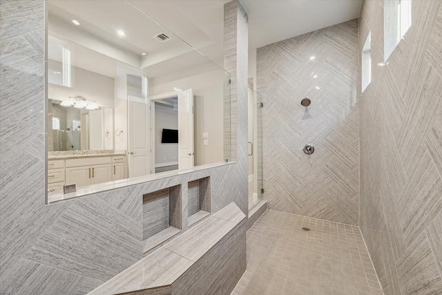 bathroom featuring vanity, a tile shower, and tile walls