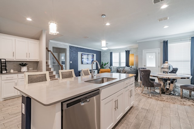 kitchen featuring stainless steel dishwasher, sink, decorative light fixtures, white cabinetry, and an island with sink