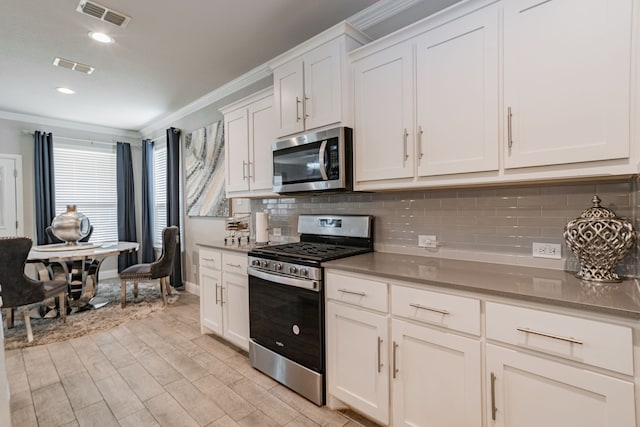 kitchen featuring decorative backsplash, light wood-type flooring, ornamental molding, stainless steel appliances, and white cabinetry