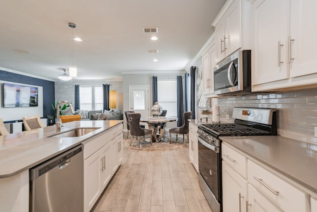 kitchen with white cabinets, stainless steel appliances, ornamental molding, and sink