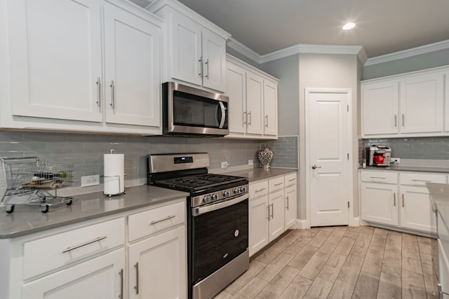 kitchen featuring light wood-type flooring, tasteful backsplash, stainless steel appliances, crown molding, and white cabinetry