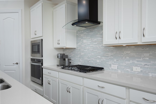 kitchen with decorative backsplash, white cabinetry, stainless steel appliances, and wall chimney range hood