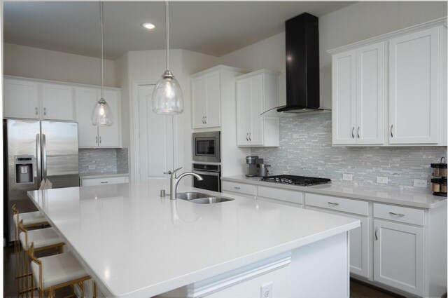 kitchen with appliances with stainless steel finishes, sink, wall chimney exhaust hood, and an island with sink