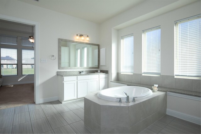 bathroom with tile patterned floors, plenty of natural light, a relaxing tiled tub, and vanity